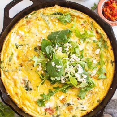 Vegetable frittata recipe in cast iron pan garnished with greens and cheese.