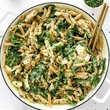 Chicken spinach pasta in a white bowl with gold utensils.