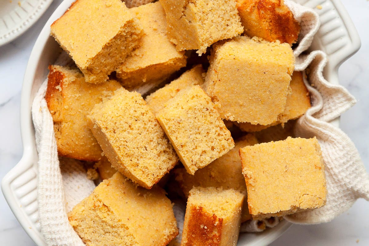 Healthy cornbread squares in a bowl with white towel.