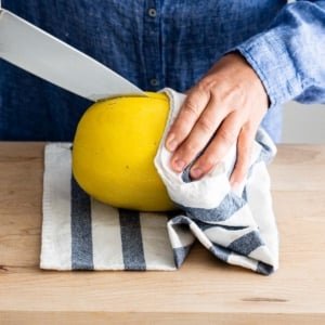 Holding spaghetti squash with a towel and inserted knife in it on a cutting board.
