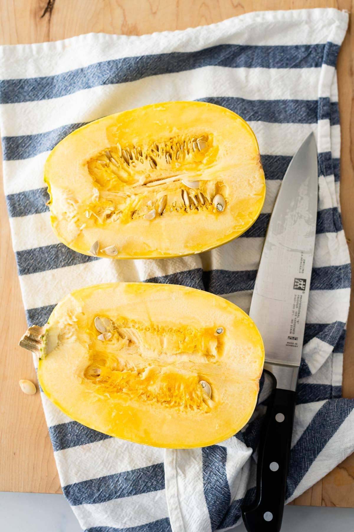 Two spaghetti squash halves on a cutting board with a knife and towel.