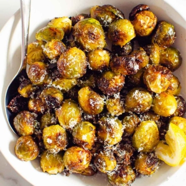 Parmesan roasted brussels sprouts in white bowl with serving spoon.