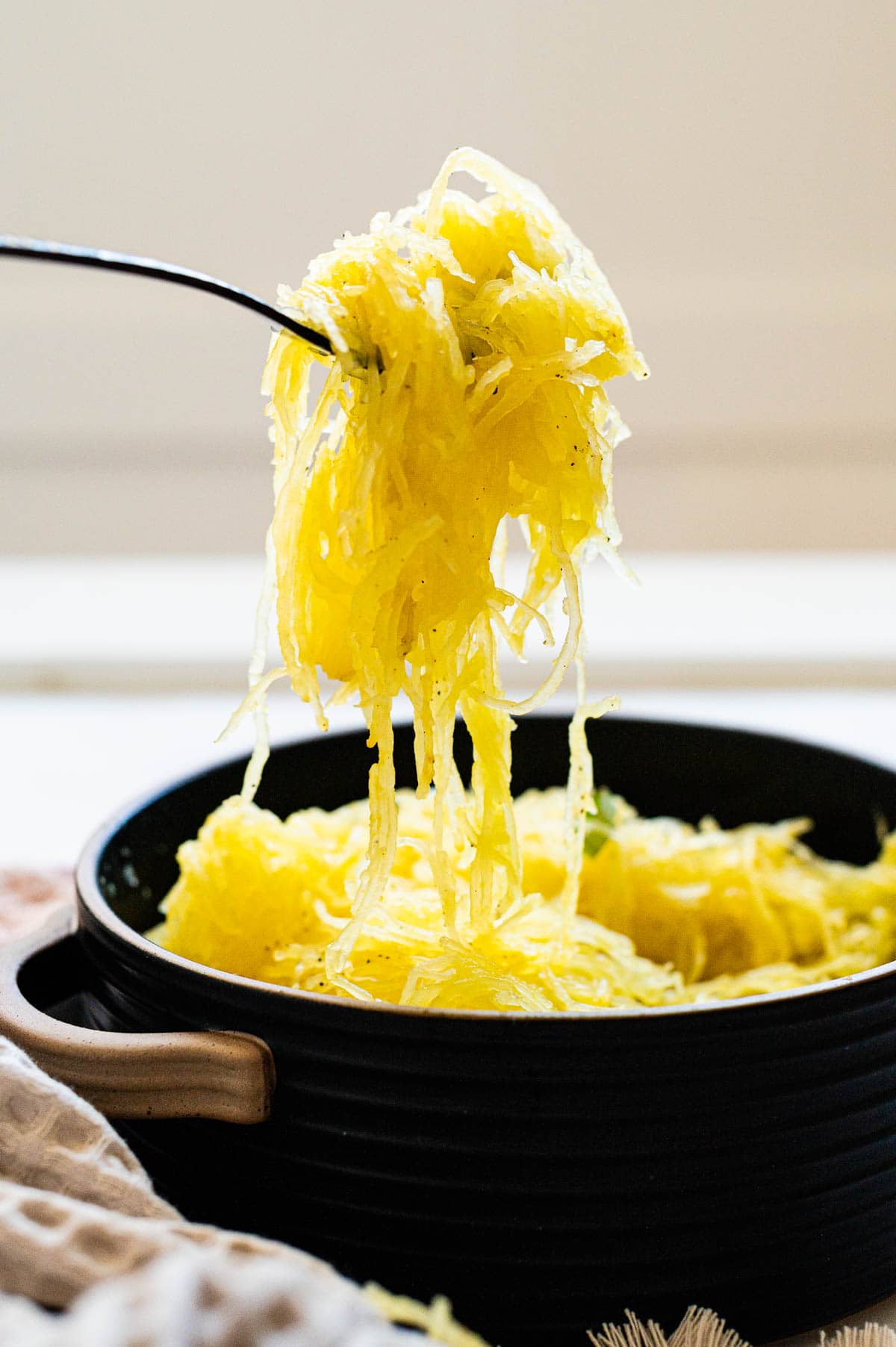 Person holding cooked spaghetti squash pasta on a fork over a bowl.