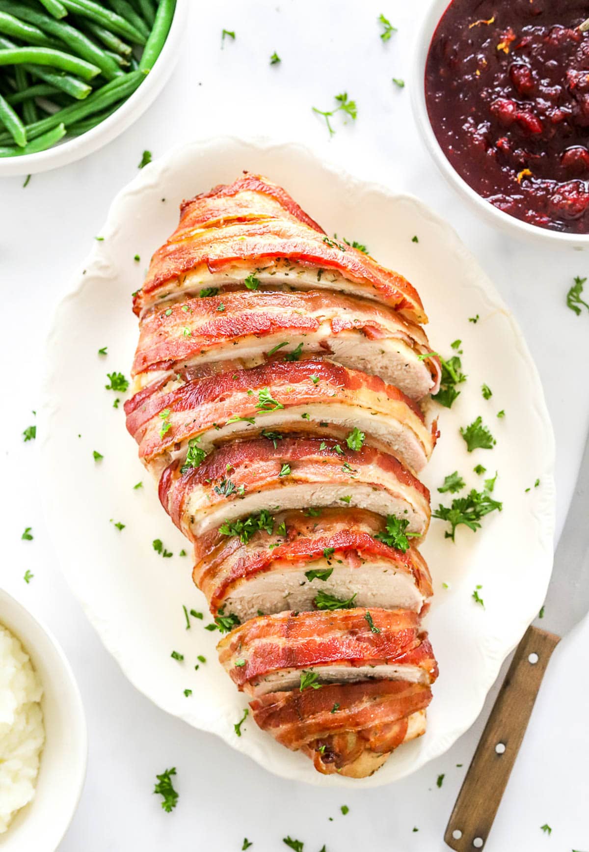 Turkey breast wrapped in bacon sliced and served on a platter with parsley garnish.