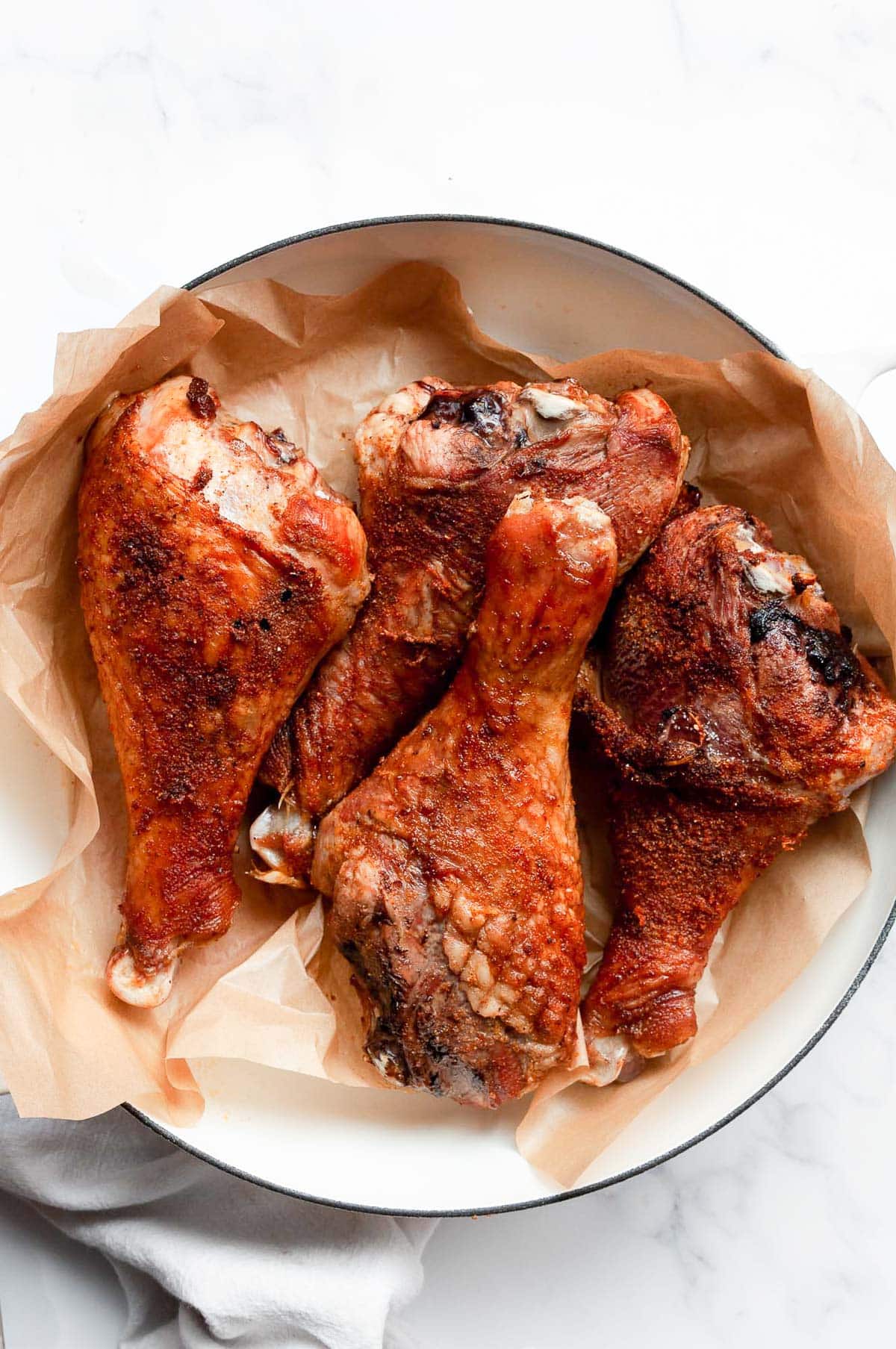 Four baked turkey legs on parchment paper in a serving dish.