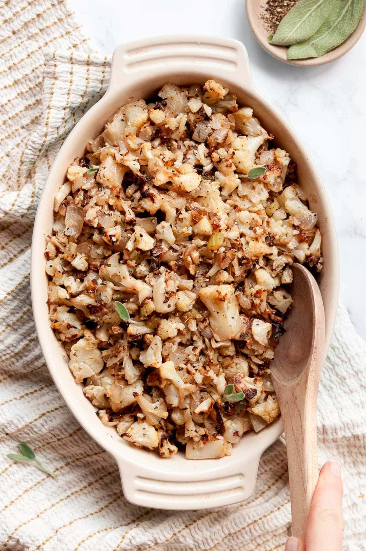 Person holding wooden spoon in a dish with cauliflower stuffing.