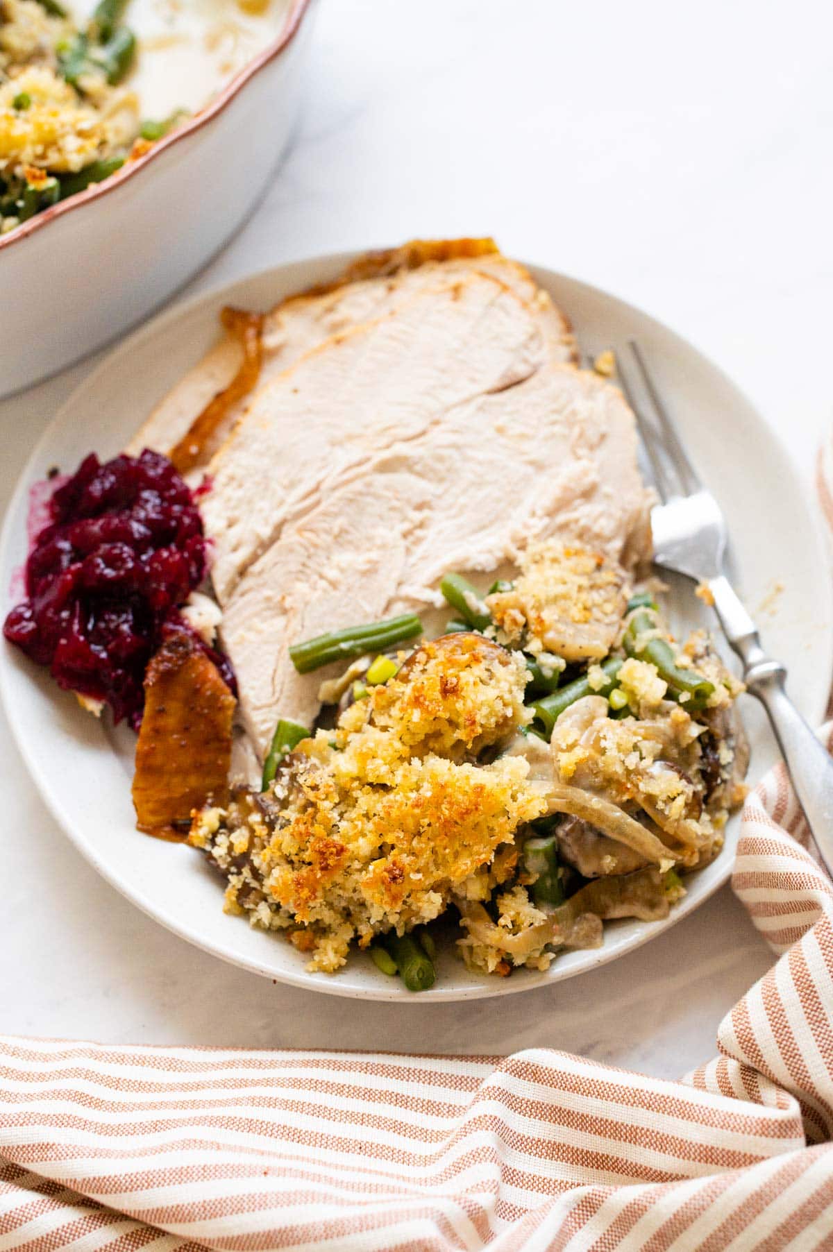 A plate with sliced turkey breast, green bean casserole and cranberry sauce.