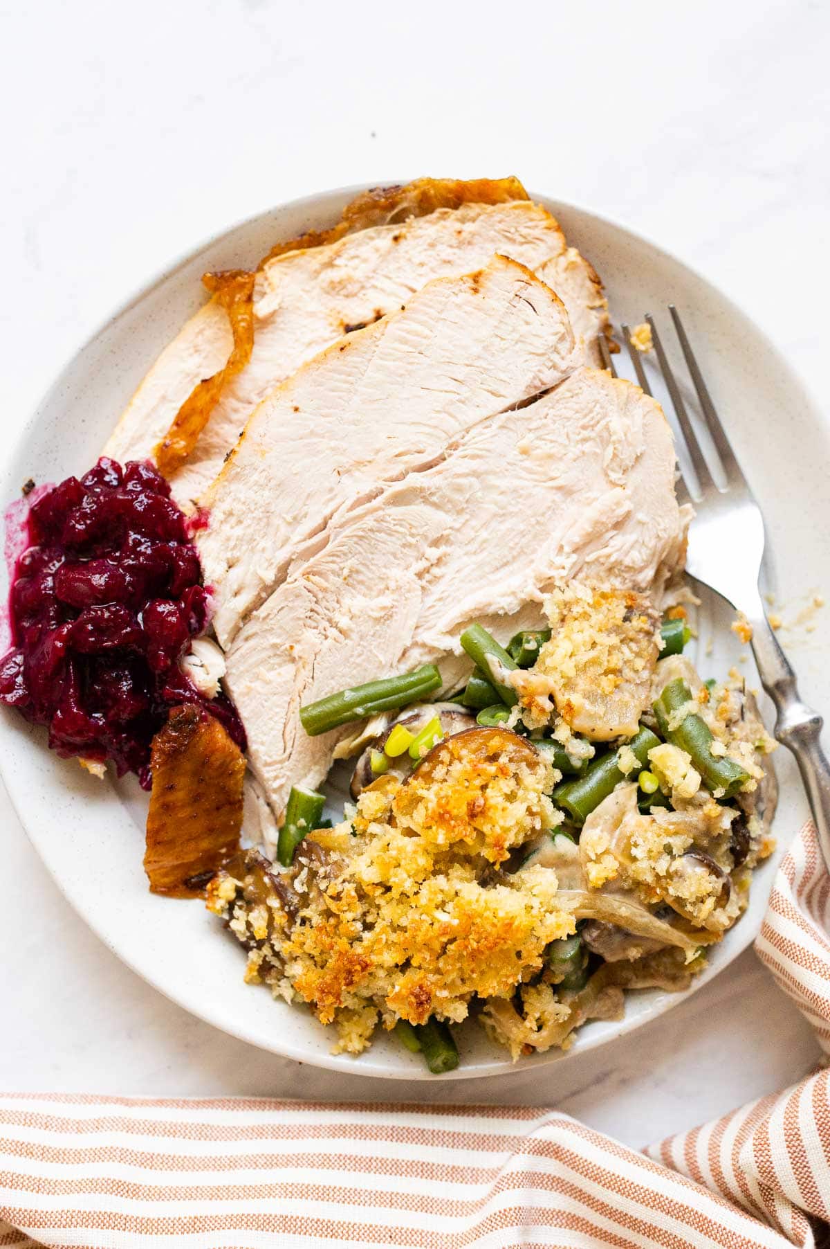Sliced turkey breast served with cranberry sauce and green bean casserole on a plate.