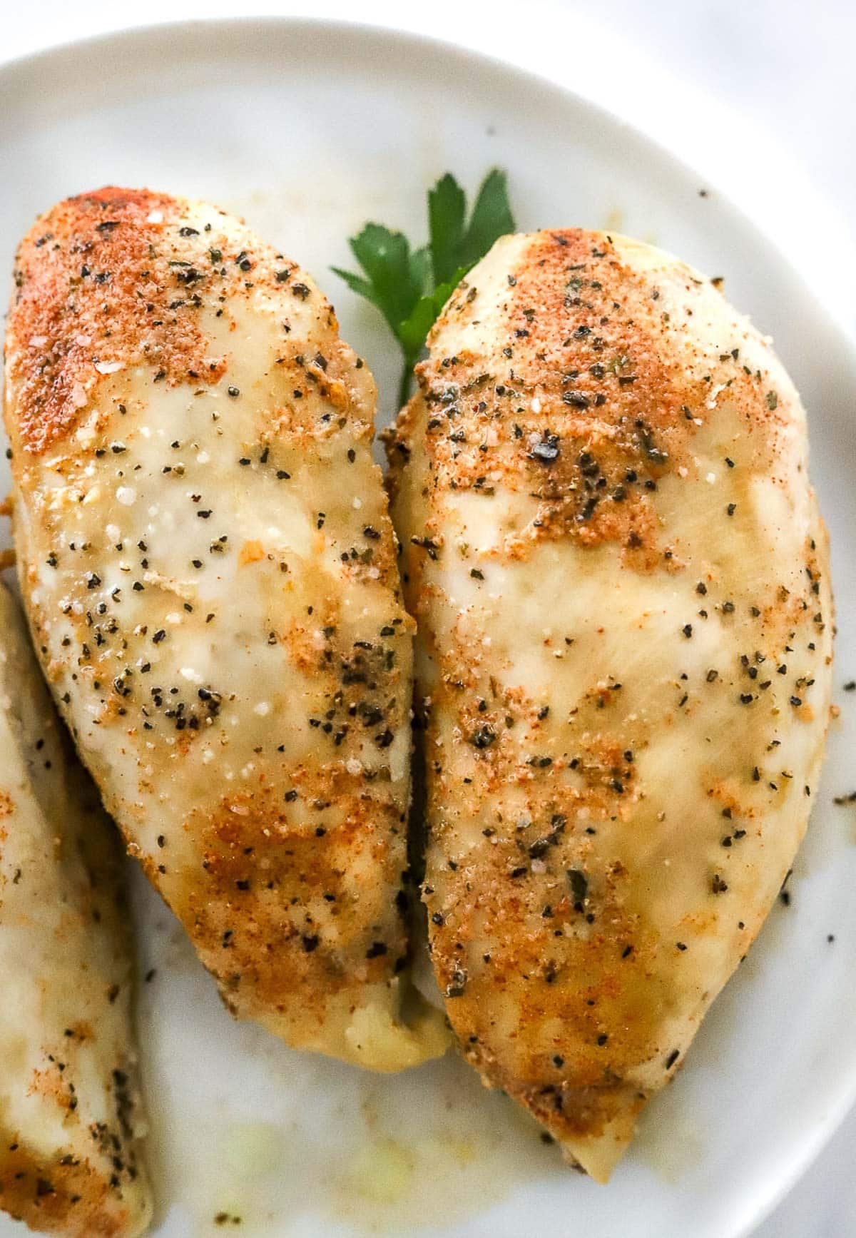 Two seasoned cooked chicken breasts in crockpot on a plate.