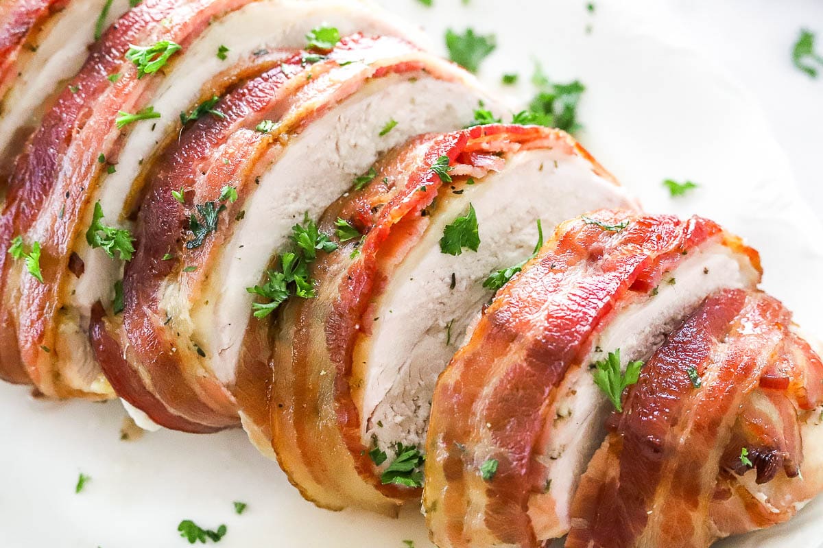 Bacon wrapped turkey breast sliced on a plate and garnished with parsley.