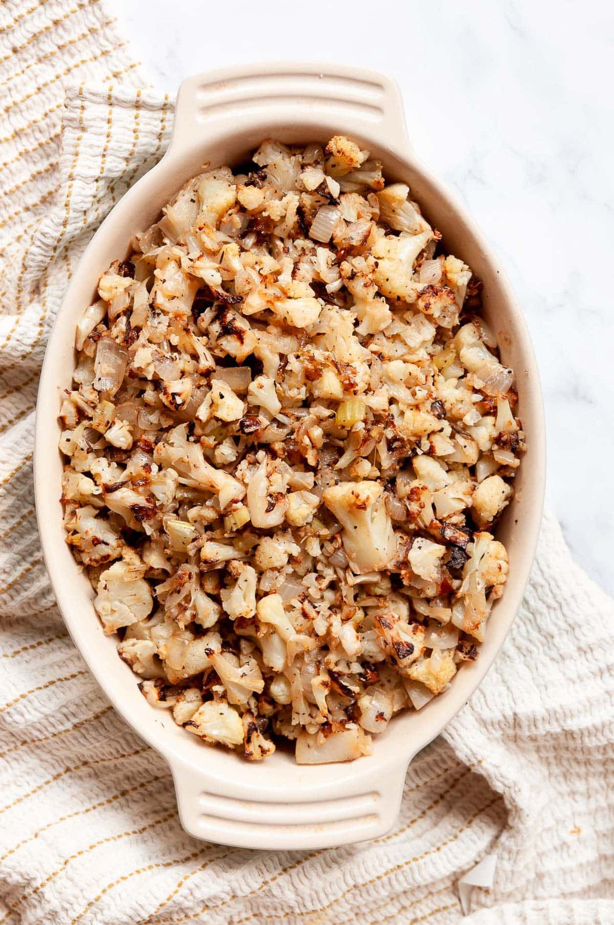 Cauliflower dressing in oval baking dish on top of towel.