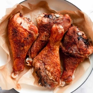 Four baked turkey legs on parchment lined serving dish.