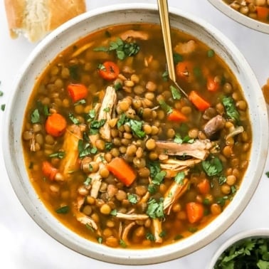 Chicken and lentil soup with carrots and parsley in a bowl with spoon.