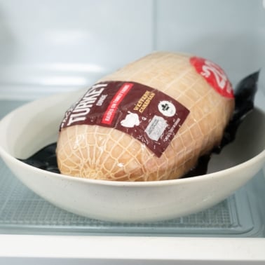 Frozen turkey breast on a plate in the refrigerator.