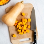 Cubed butternut squash on a cutting board with a knife and whole squash.