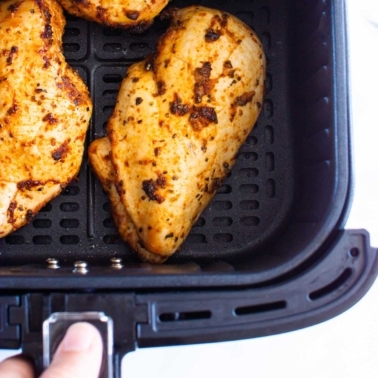 Person holding air fryer basket with cooked chicken breasts in it.