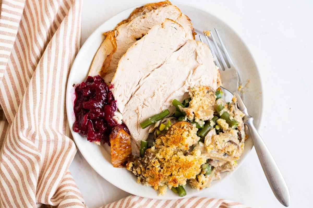 Sliced turkey breast with green bean casserole and cranberry sauce served on a plate.