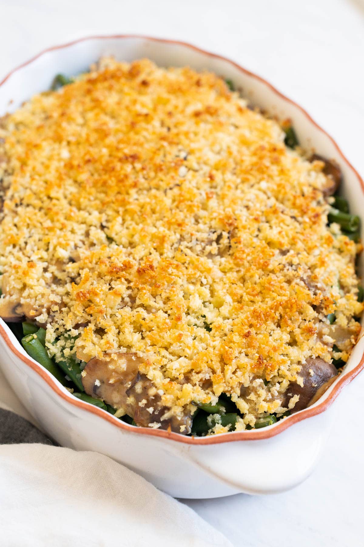 Healthy green bean casserole with parmesan breadcrumb topping in white dish.