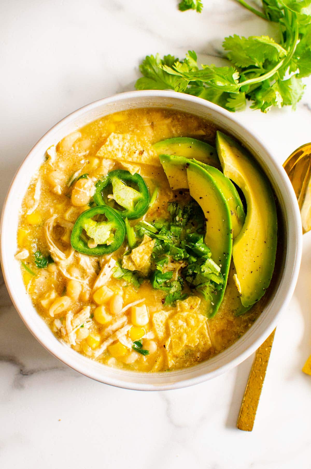 A bowl with healthy white chicken chili and garnishes.