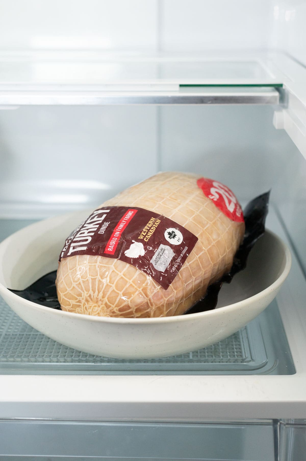 Frozen turkey breast roast in original wrapper on a plate in the fridge.