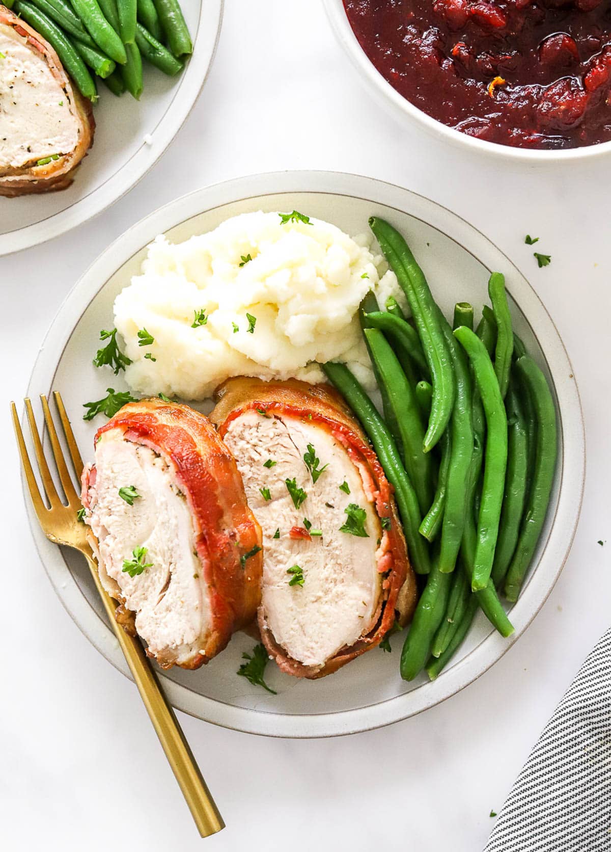 A plate with sliced turkey breast, mashed potatoes and green beans. Cranberry sauce in a bowl.