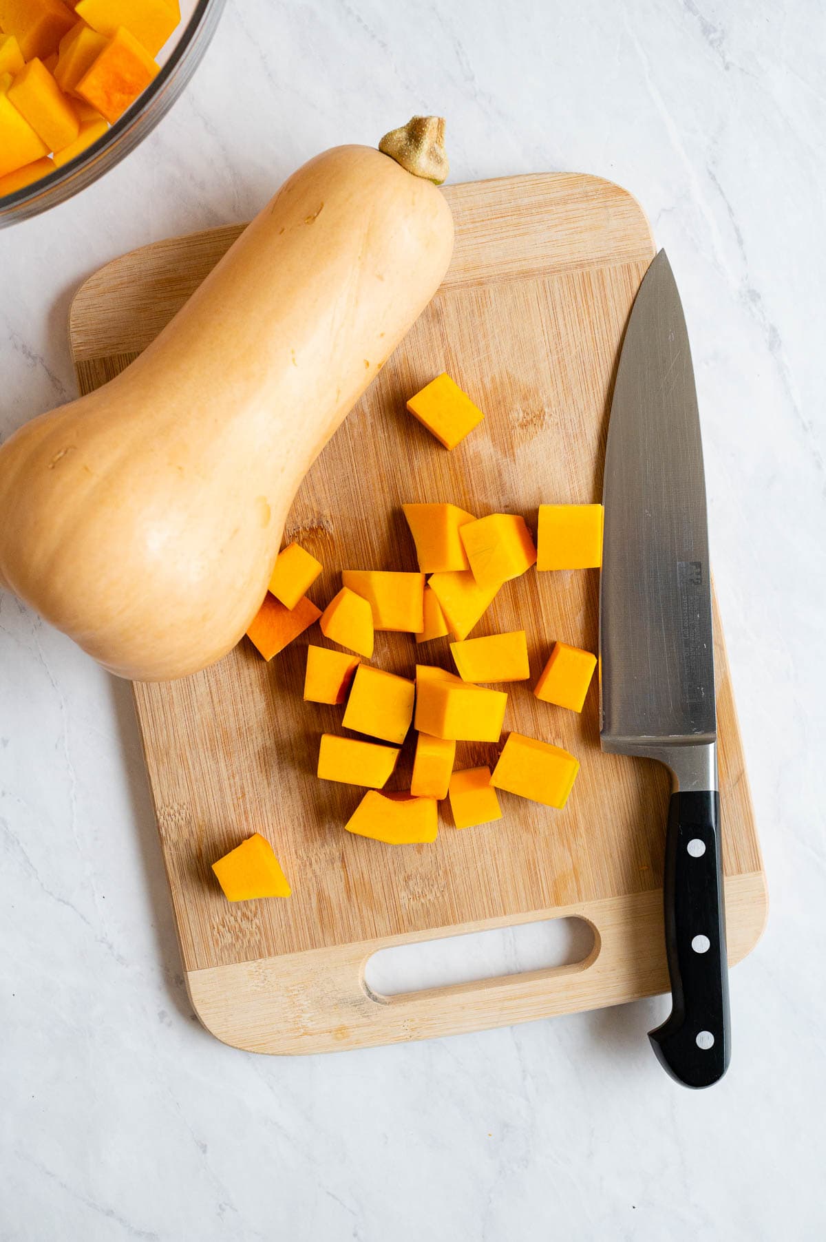 Cubed butternut squash on a cutting board with a knife and whole squash.