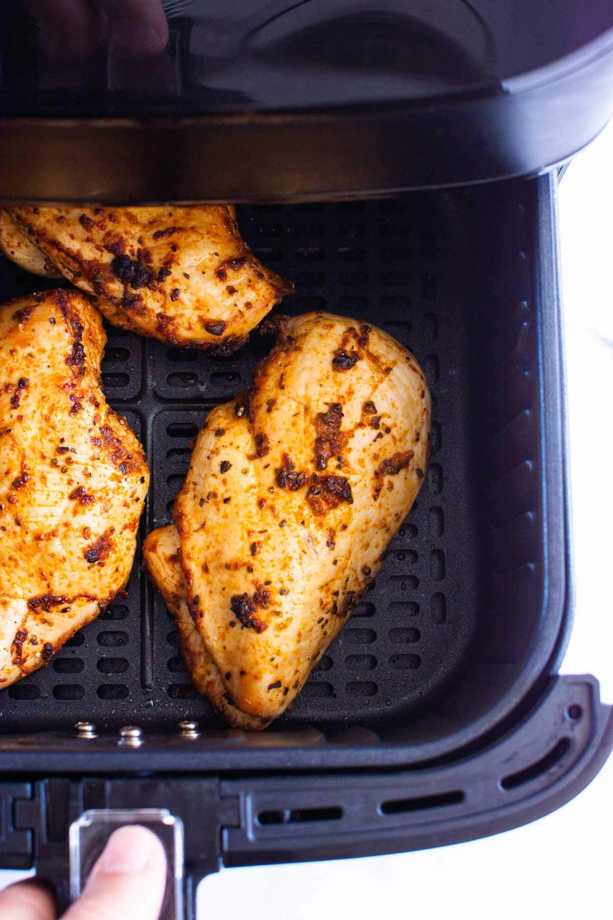 Three cooked chicken breasts in air fryer basket.