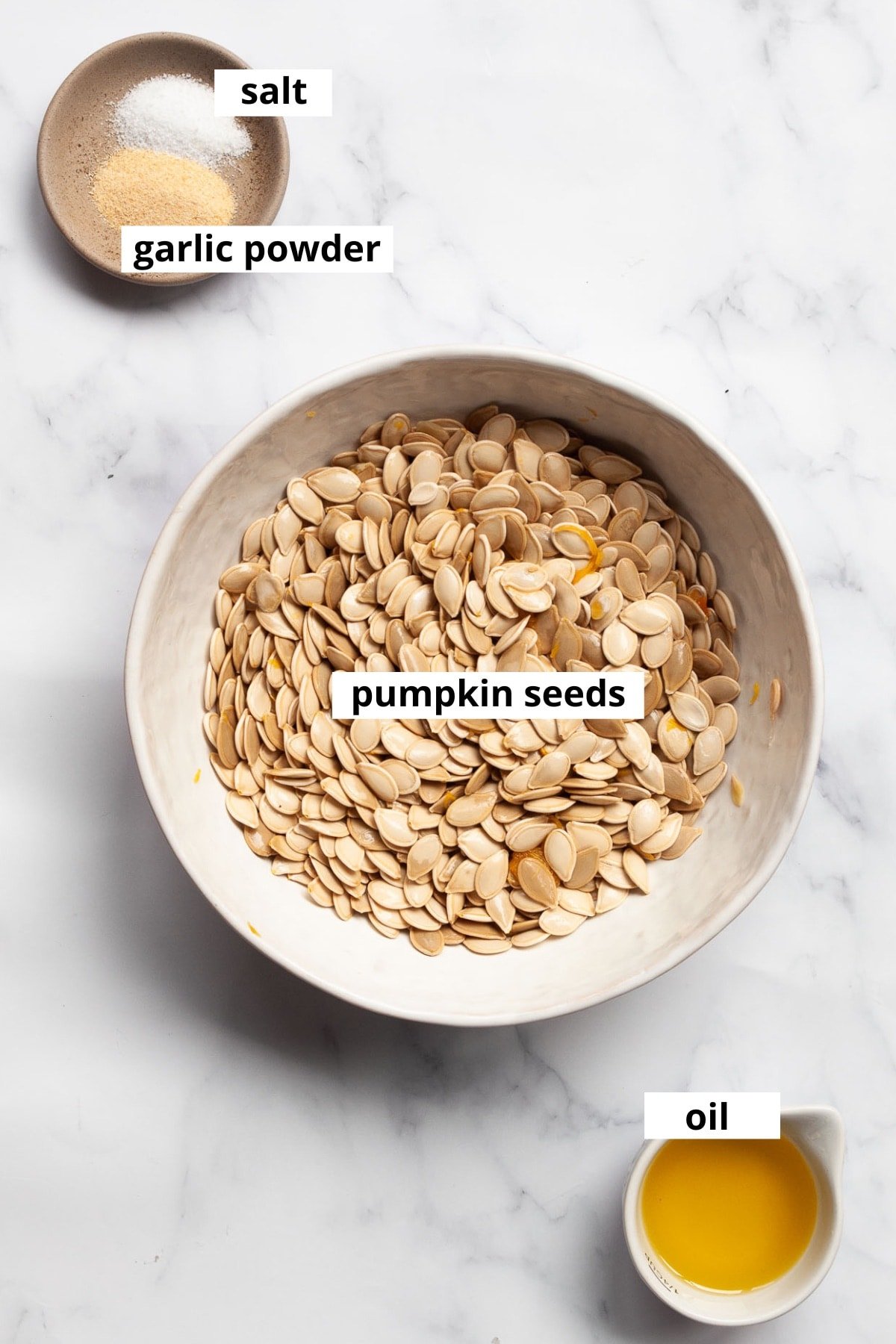 Raw pumpkin seeds in a bowl, oil, garlic powder and salt.