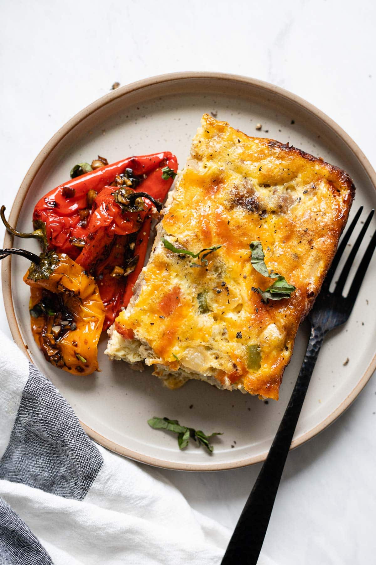 A slice of low carb breakfast casserole with roasted mini peppers on a plate with a fork.