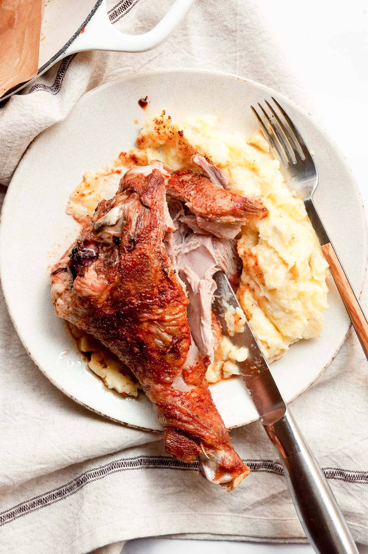 Oven roasted turkey leg showing meat texture and mashed potatoes with a knife and fork on a plate.