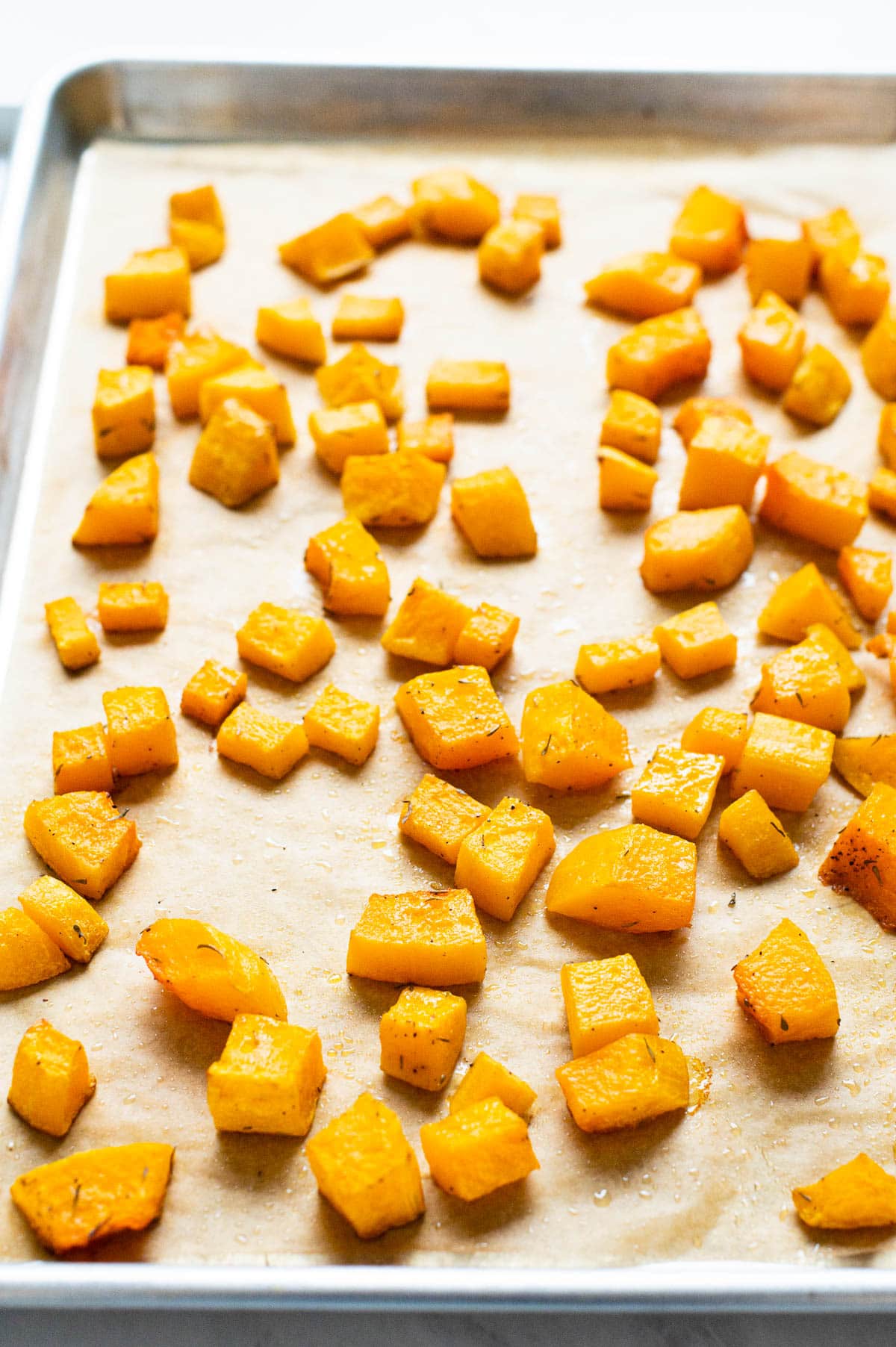 Roasted butternut squash cubes on parchment lined baking sheet.