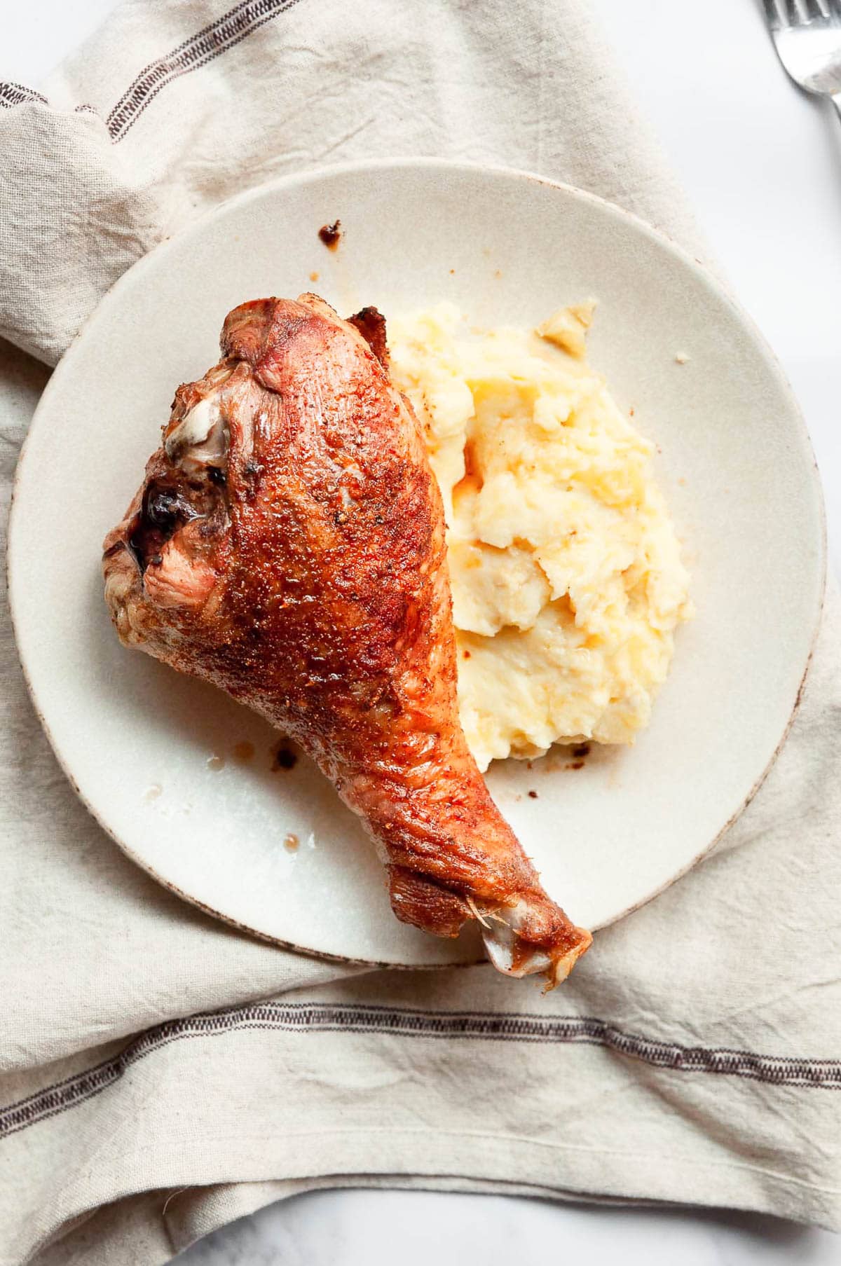 Baked turkey drumstick with mashed potatoes on a plate on top of linen towel.