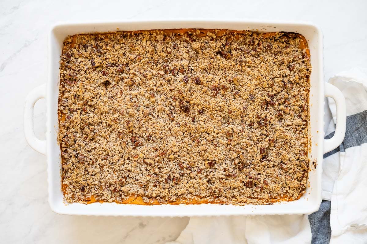 Sweet potato casserole with pecan crumb topping in white baking dish and linen towel.