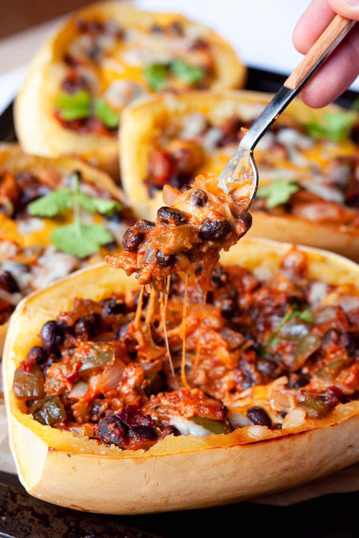 Stuffed spaghetti squash with beans, cheese and sauce on a fork above the squash halves.