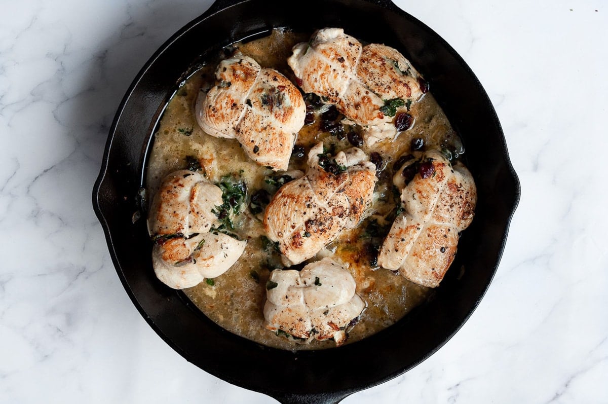 Brie stuffed chicken in cast iron skillet with wooden spoon and pan juices.