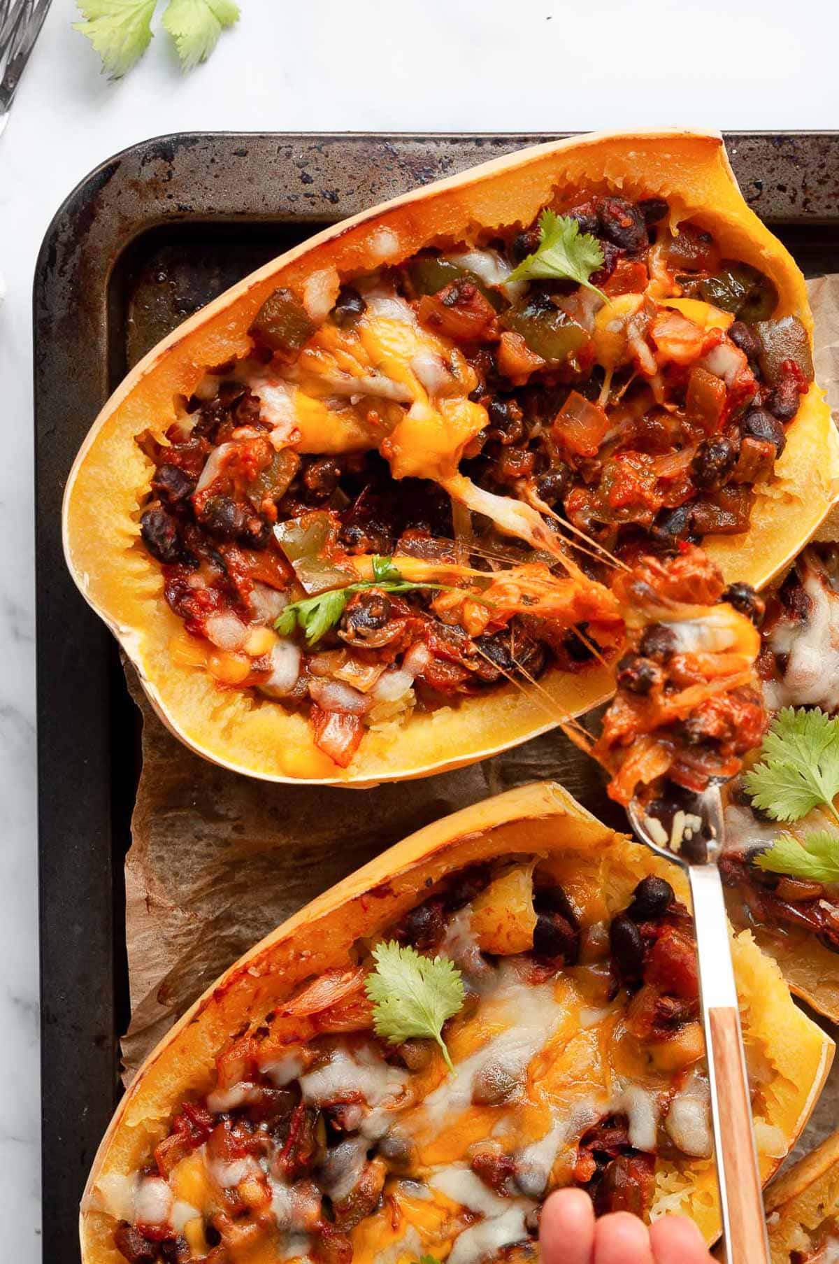 Person pulling the cheesy stuffing from the squash half with a fork.