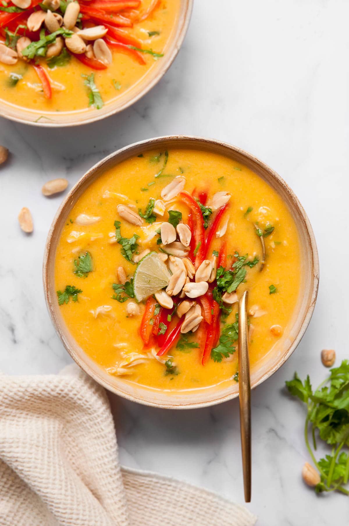 Butternut squash soup with chicken, red peppers, peanuts, lime, and cilantro in a bowl with a spoon.