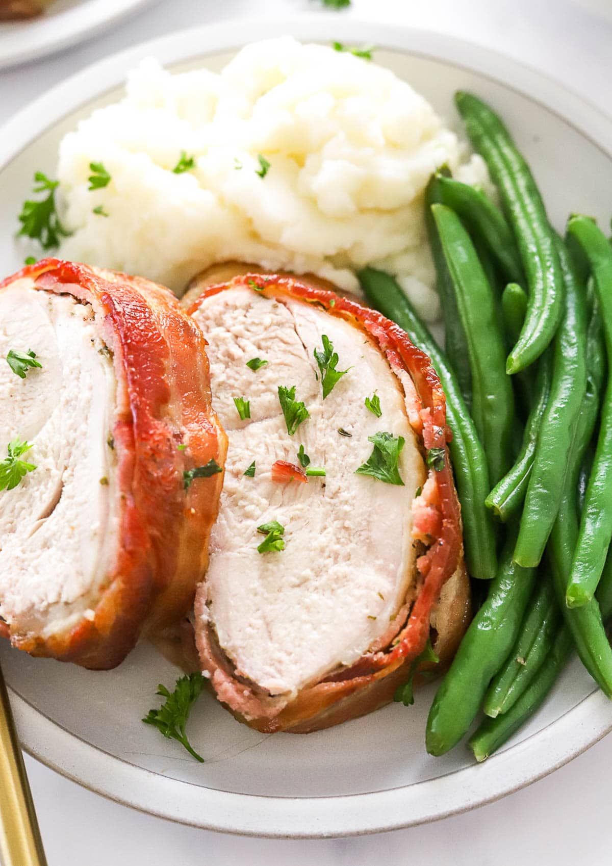 Sliced bacon wrapped turkey breast served with mashed potatoes and green beans.