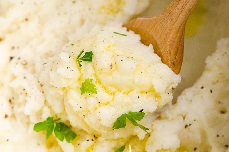 Closeup of mashed potatoes scooped with wooden spoon and garnished with parsley.