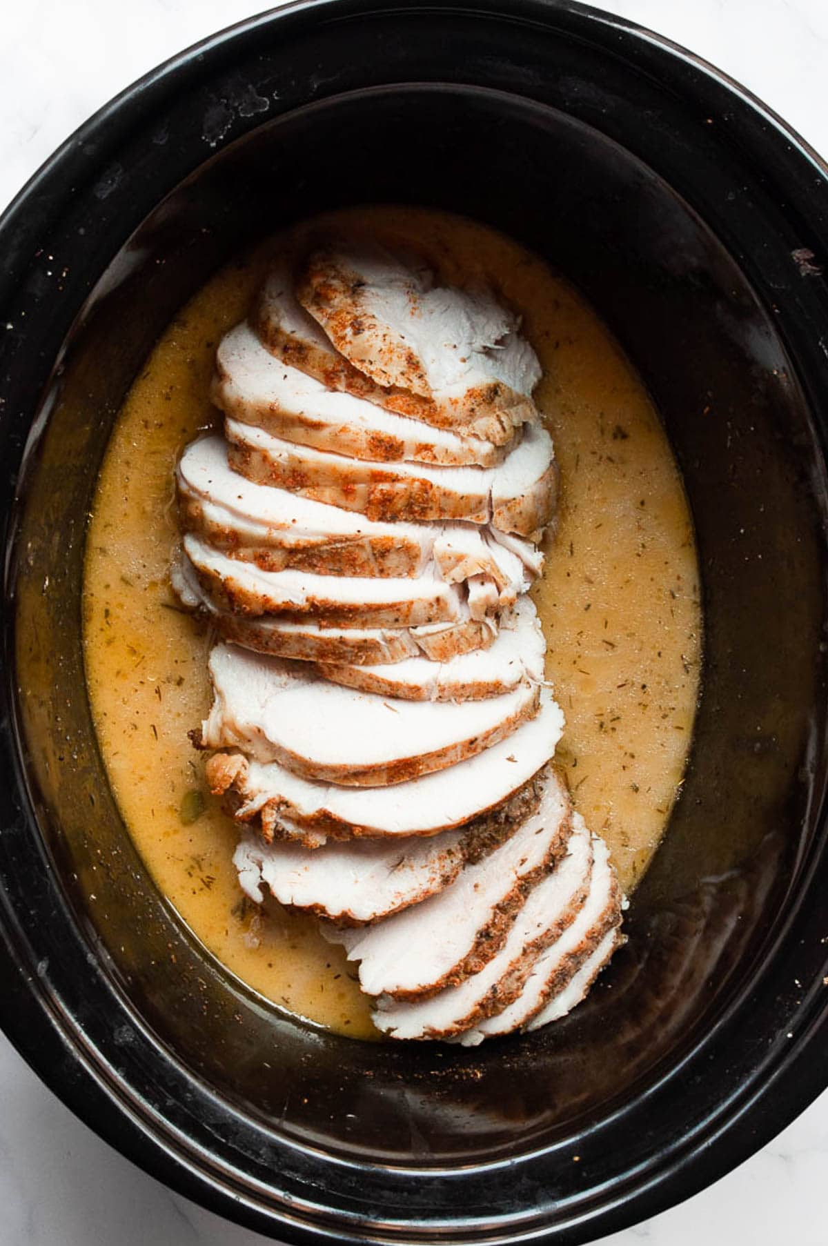 Sliced turkey breast with gravy in slow cooker.