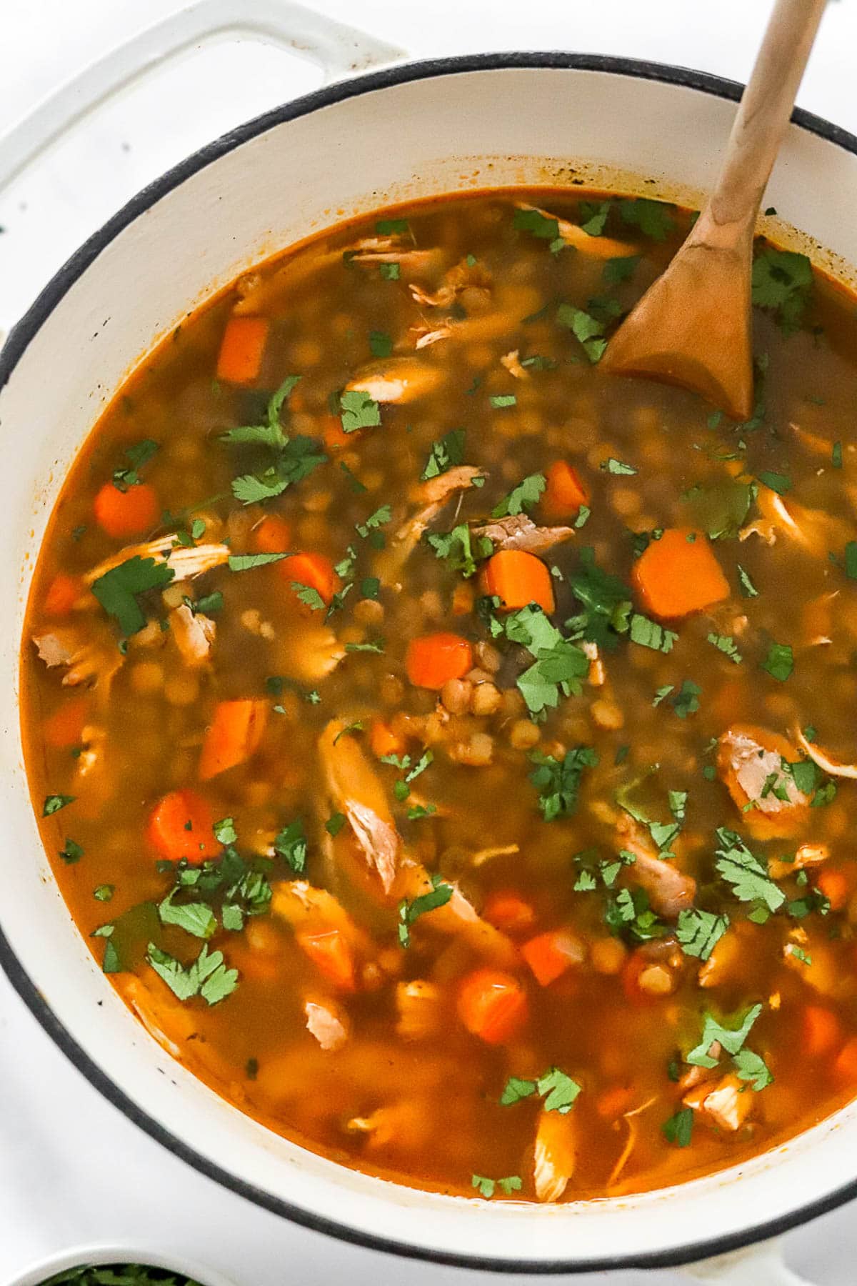 Chicken lentil soup in a pot with wooden spoon.