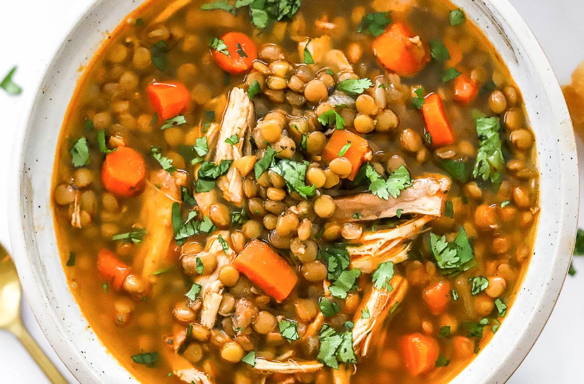 Chicken and lentil soup with carrots and cilantro served in white bowl.