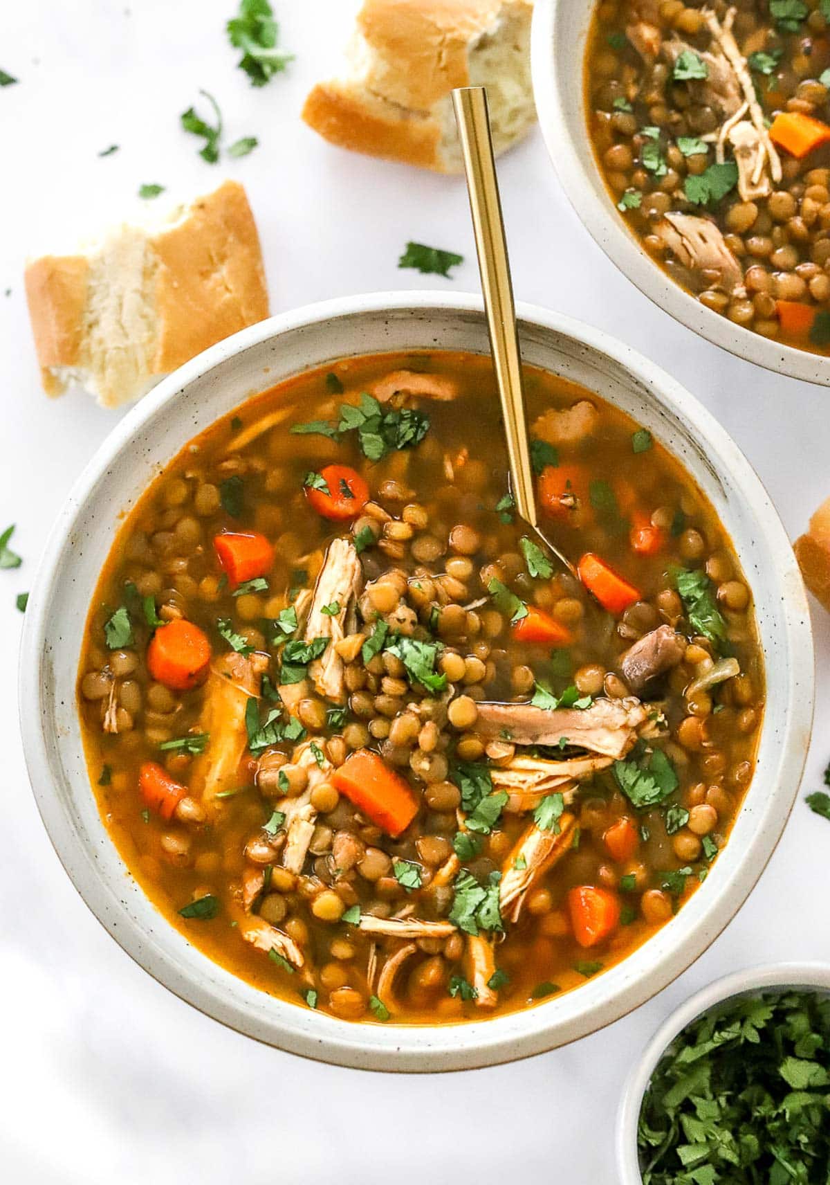 Chicken and lentil soup with carrots and parsley in a bowl with spoon.