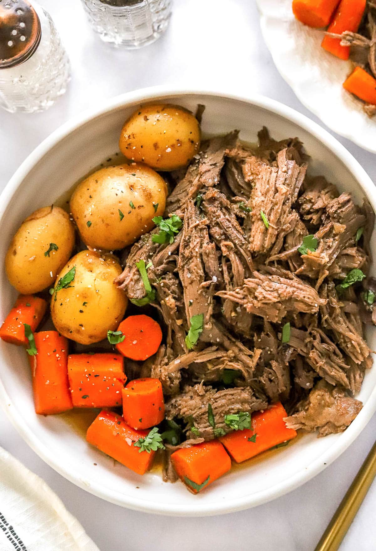 Shredded rump roast served with carrots and baby potatoes in white bowl.