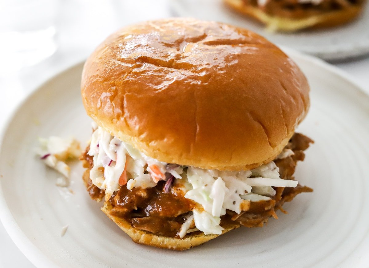 Pulled pork sandwich on brioche bun with coleslaw on white plate.