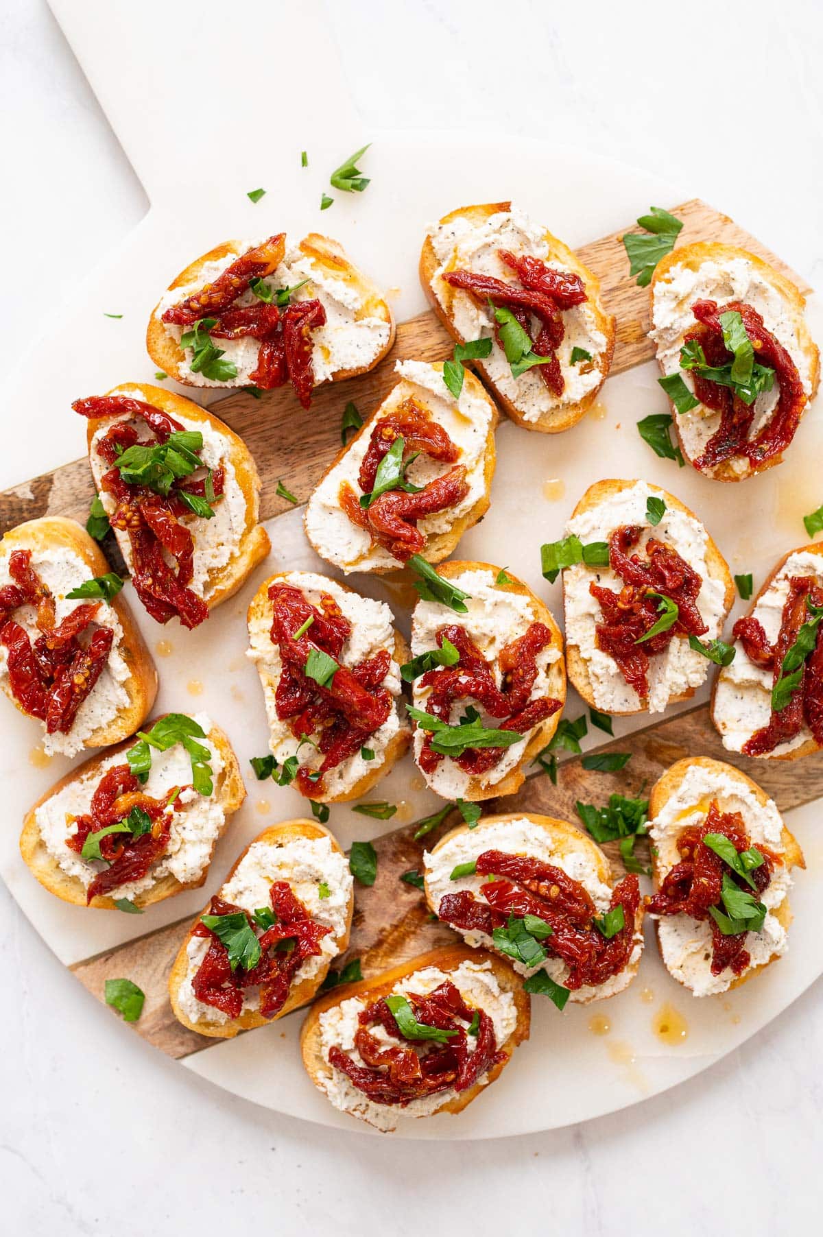 Crostini appetizers with sun dried tomatoes and parsley on marble board.