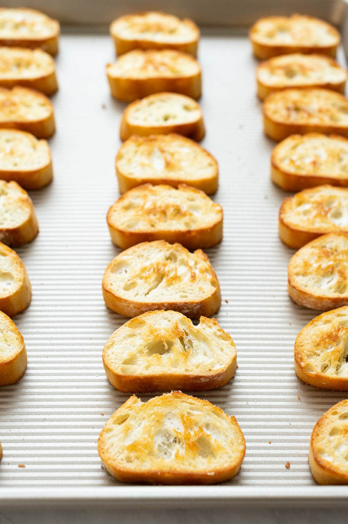 Lined up in rows baked crostini on a baking sheet.