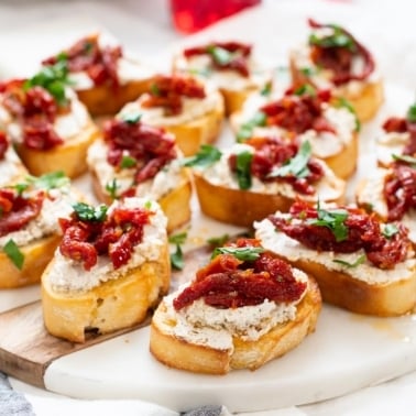 Goat cheese crostini with sun dried tomatoes on marble serving platter.