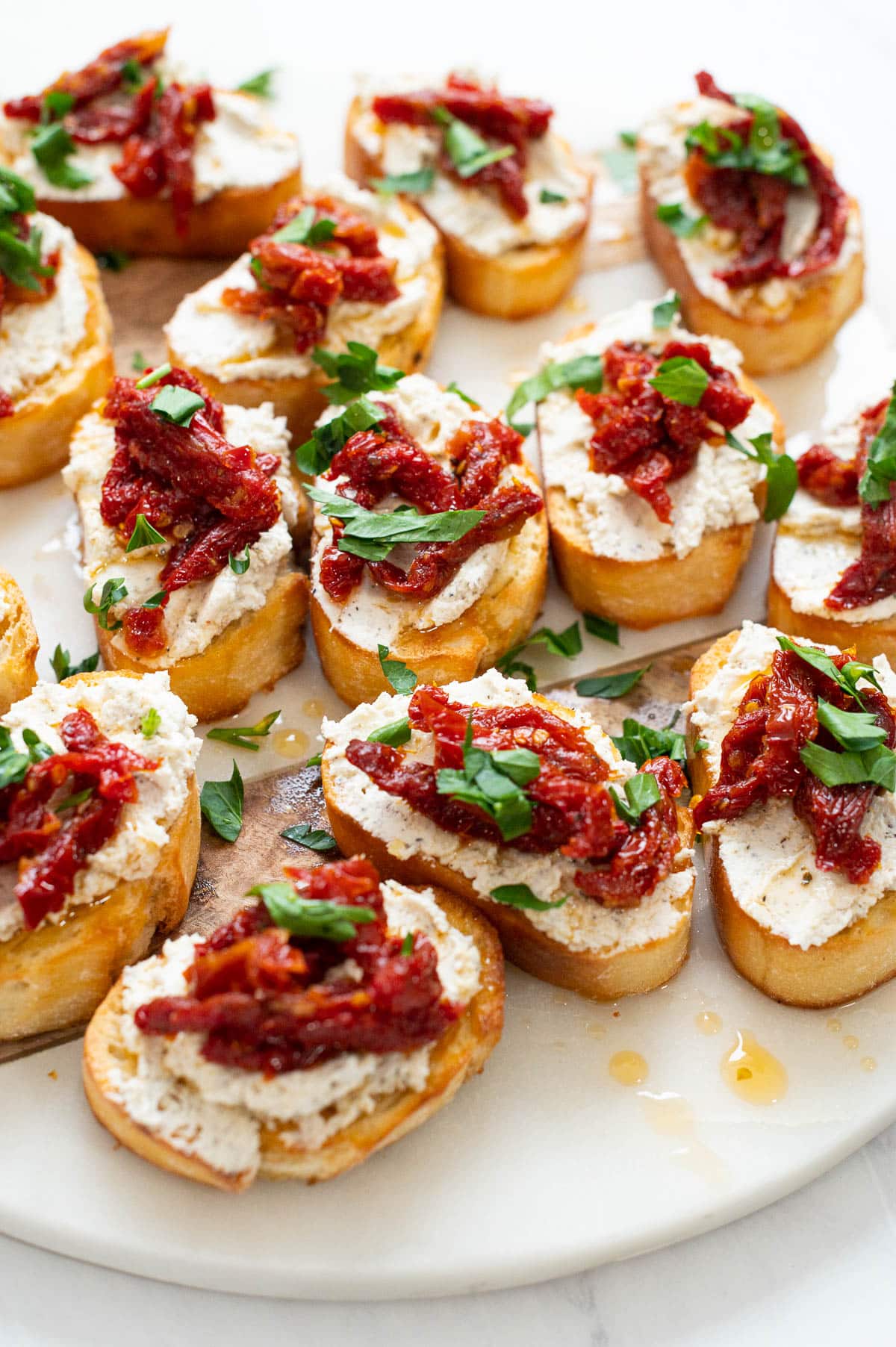 Goat cheese crostini with sun dried tomatoes on marble serving platter.