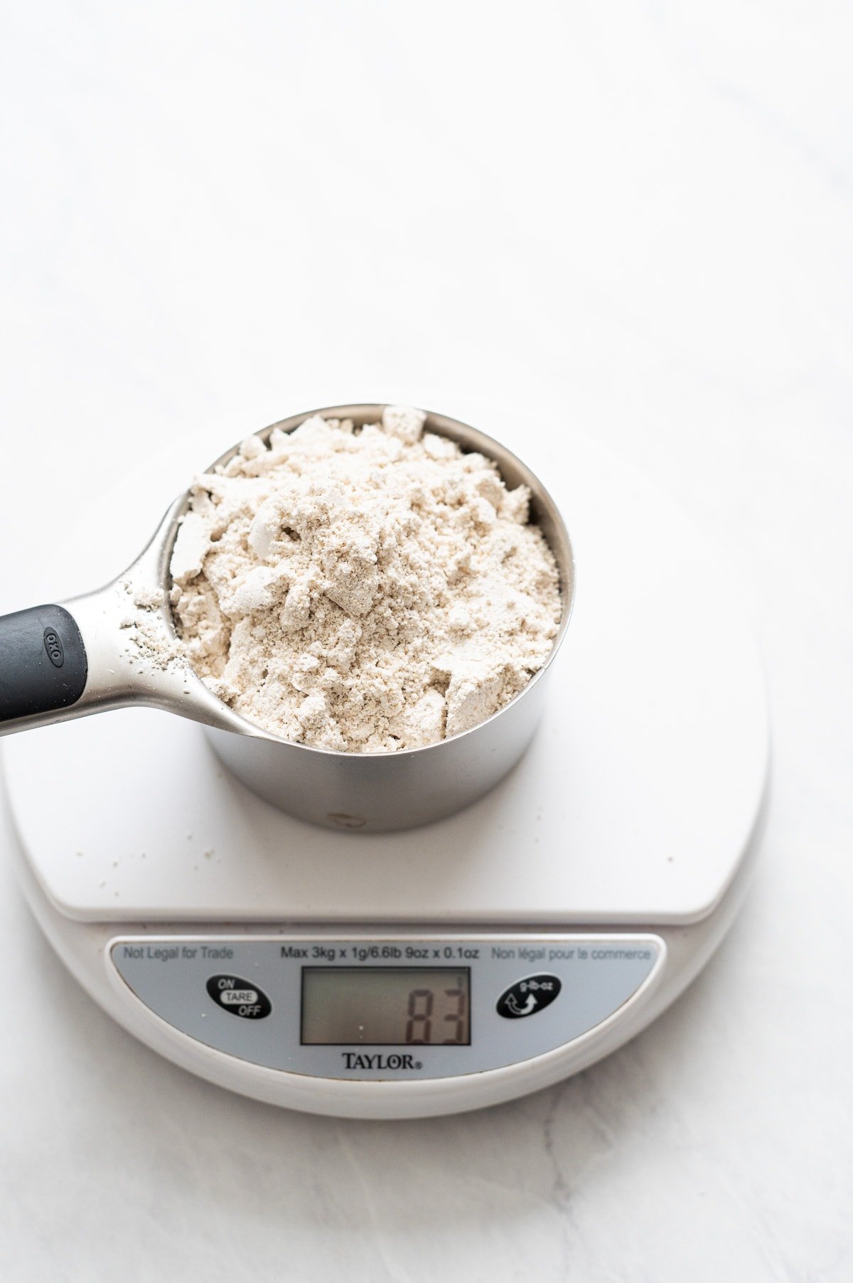 Oats in a measuring cup on a kitchen scale showing 83 grams.